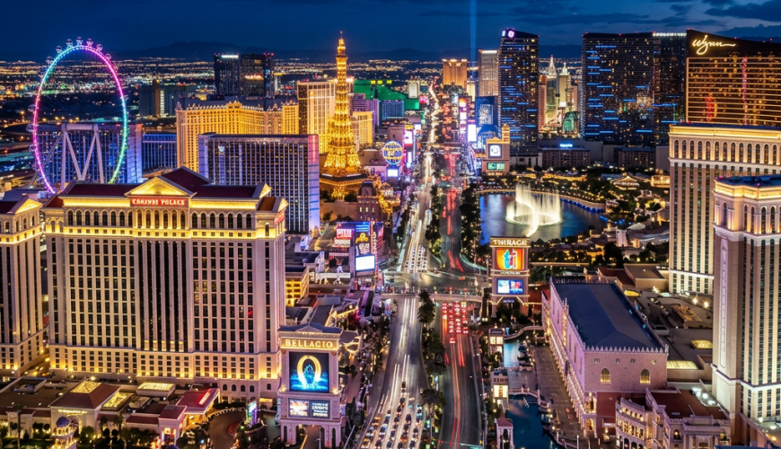 Aerial view of the Las Vegas Strip at night with bright city lights, hotels, and a large ferris wheel